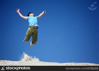 boy jumps on sand with lifted hands