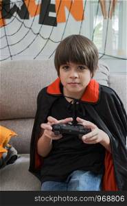 boy kids smiling and dress up as Halloween vampire costume holding joystick to play Halloween game in living room at home
