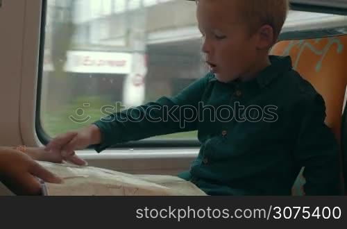 Boy learning to use map. He traveling by train and searching places on the map, mother helps him