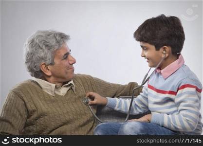 Boy listening to grandfather's heartbeat with stethoscope