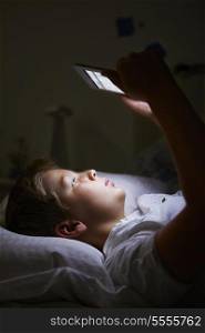 Boy Looking At Digital Tablet In Bed At Night