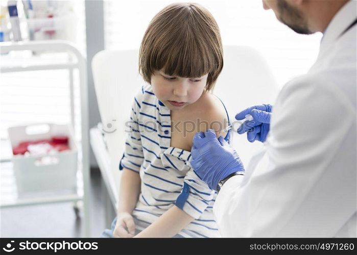 Boy looking at doctor injecting syringe in hospital