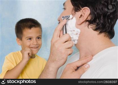 Boy looking at his father shaving in the bathroom