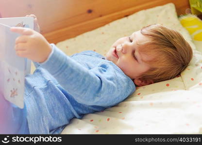 Boy lying on back in bed looking at storybook