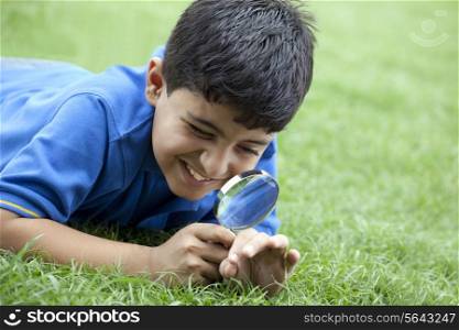 Boy lying on grass using magnifying glass