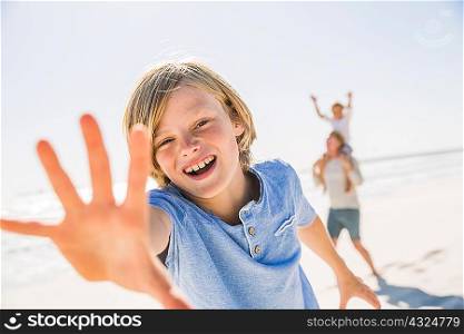 Boy on beach looking at camera, hand raised smiling
