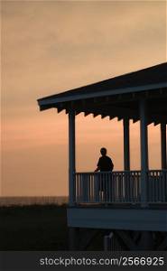 Boy on beachfront porch silhouetted at sunset