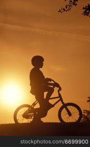 Boy On Bicycle Silhouetted By Sunset