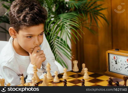 Boy playing chess at home. Sitting at the table and thinking hard.