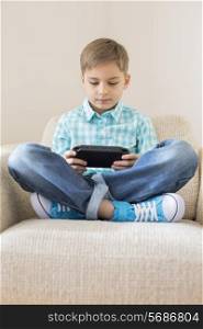 Boy playing hand-held video game on sofa at home