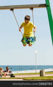 Boy playing swinging by swing-set.. Rest and relax for children. Little boy in sunglasses resting swinging outdoor. Adorable child having fun playing in playground.