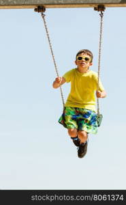 Boy playing swinging by swing-set.. Rest and relax for children. Little boy in sunglasses resting swinging outdoor. Adorable child having fun playing in playground.