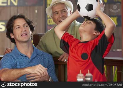 Boy playing with a soccer ball with his father and grandfather looking at him