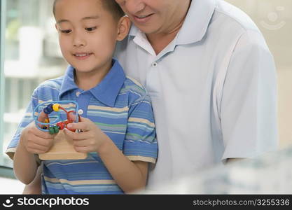 Boy playing with a toy and his grandfather standing behind him