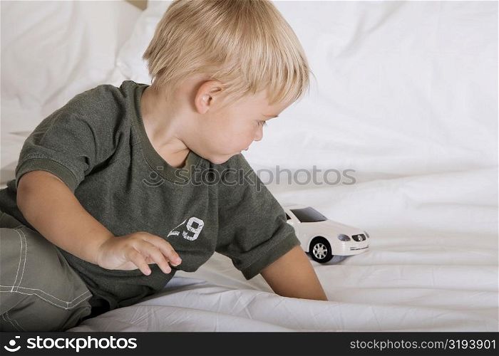 Boy playing with a toy car on a bed