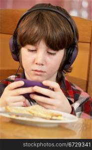 Boy Playing With Hand Held Games Console Whilst Eating Breakfast