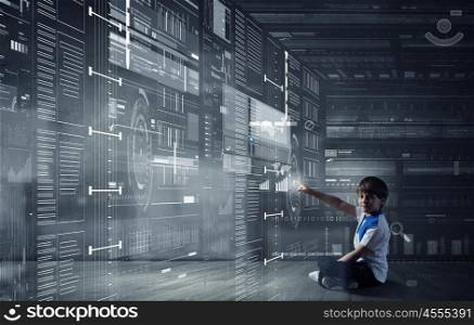 Boy pointing at virtual planet. Cute school boy sitting on floor and touching digital screen with finger
