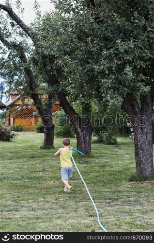 Boy pulling a garden hose to watering the plants in backyard garden. Candid people, real moments, authentic situations