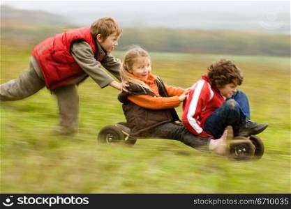 Boy pushing a mountain board with his friends sitting on it