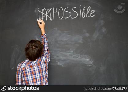 boy putting a cross over impossible on blackboard. success and challenge concept