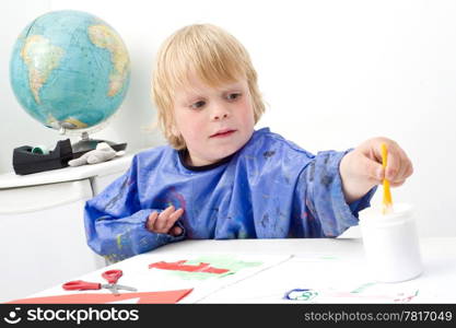Boy reaching for the jar of glue with a small brush