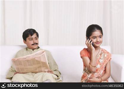Boy reading newspaper and while girl talks on mobile phone