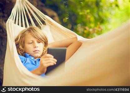 Boy reclining in garden hammock browsing digital tablet