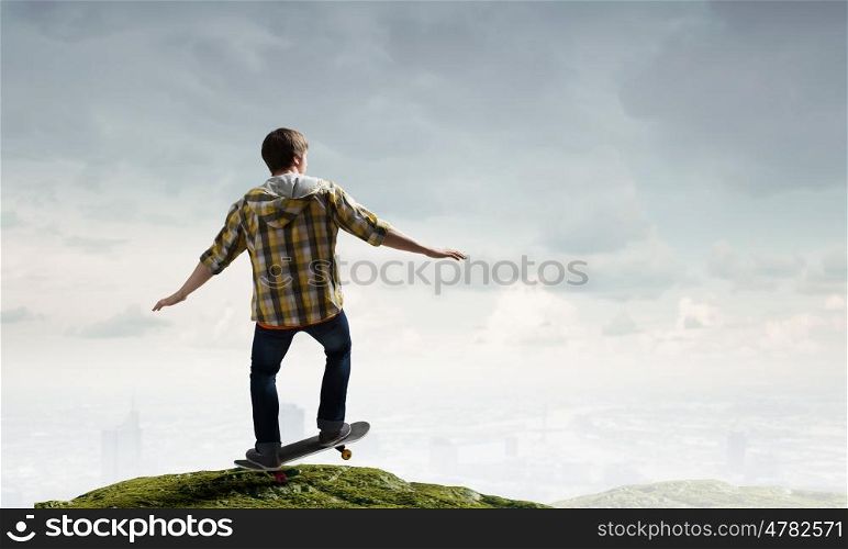 Boy ride skateboard. Active guy riding skateboard on rock edge