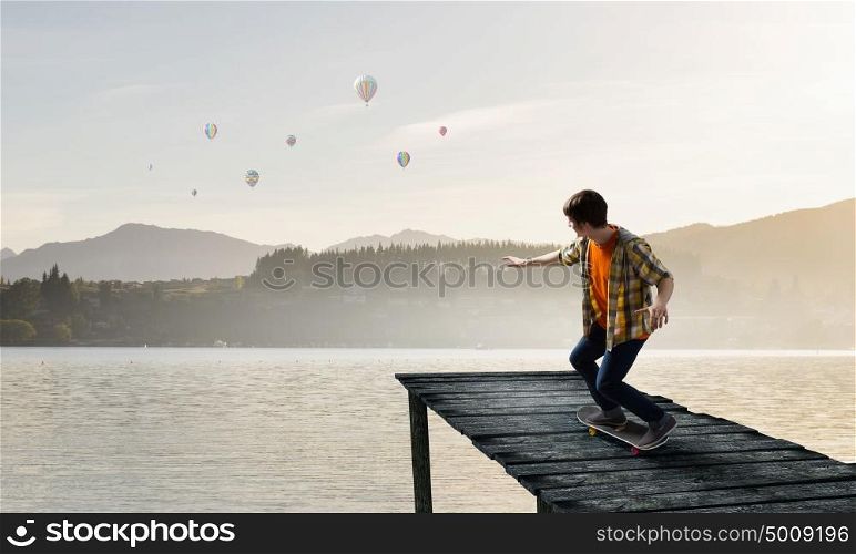 Boy ride skateboard. Active guy riding skateboard on wooden pier