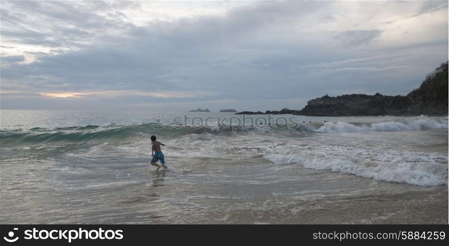 Boy running in waves on beach, Zihuatanejo, Guerrero, Mexico