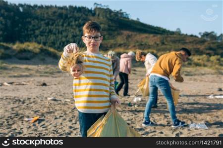Boy showing doll head with disgust face while volunteer group cleans the beach. Boy showing doll head while cleaning the beach