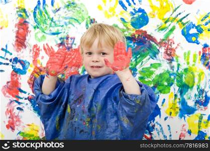 Boy showing his hands covered with red finger paint in front of his work of art
