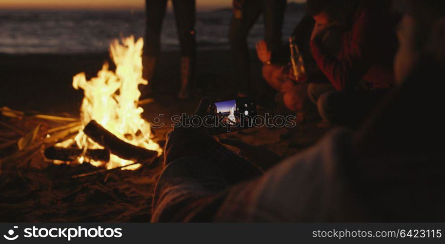 Boy Shows Girl A Picture On His Phone beside campfire on beach