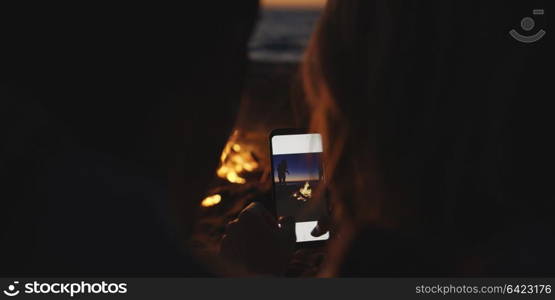 Boy Shows Girl A Picture On His Phone beside campfire on beach