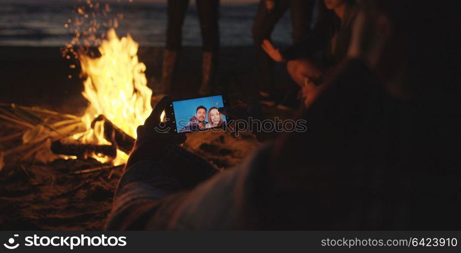 Boy Shows Girl A Picture On His Phone beside campfire on beach