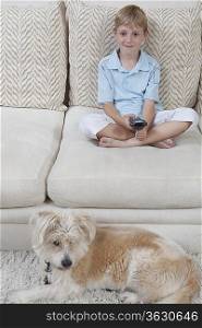 Boy sits on sofa with pet dog watching television