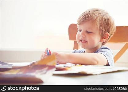Boy sitting at table holding crayons, looking away smiling