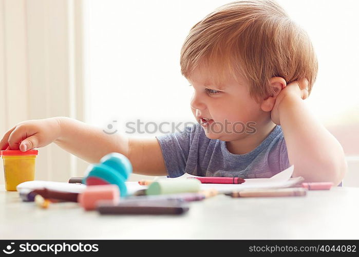 Boy sitting at table leaning on elbow looking at art supplies