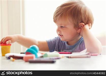 Boy sitting at table leaning on elbow looking at art supplies