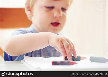 Boy sitting at table touching crayon, focus on foreground