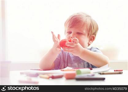 Boy sitting at table with art supplies playing with modelling clay
