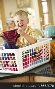 Boy Sitting In Basket Sorting Laundry On Kitchen Counter