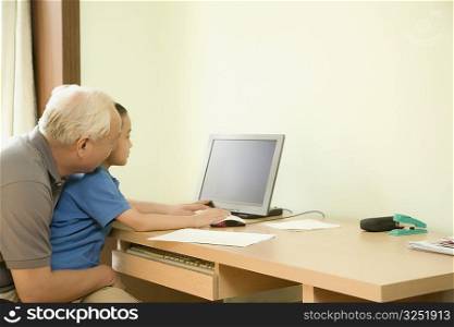Boy sitting in his grandfather&acute;s lap and working on a computer