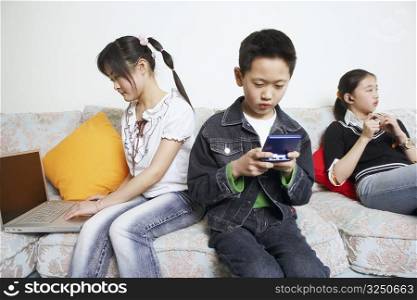 Boy sitting on a couch playing a video game beside his two sisters