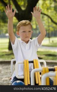 Boy sitting on a ride with his arms raised in a park