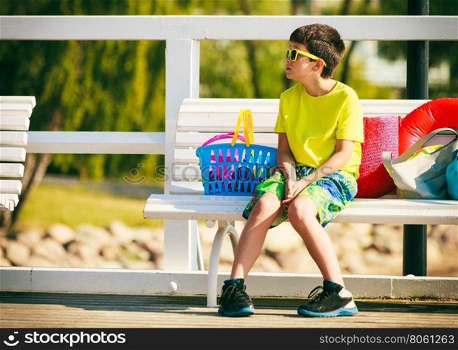 Boy sitting on bench with toys.. Active time on holidays concept. Young little boy sitting on white bench outdoor. Kid child with toys on summer holiday time.