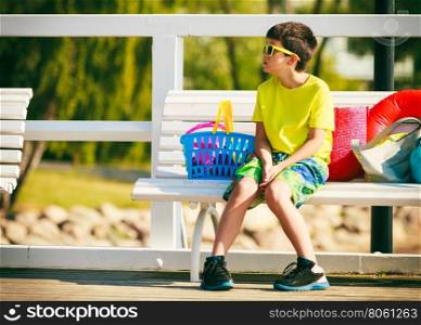 Boy sitting on bench with toys.. Active time on holidays concept. Young little boy sitting on white bench outdoor. Kid child with toys on summer holiday time.