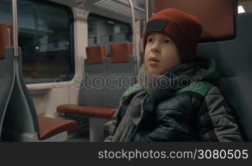 Boy sitting quietly in moving suburban train. Traveling in winter evening