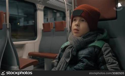 Boy sitting quietly in moving suburban train. Traveling in winter evening