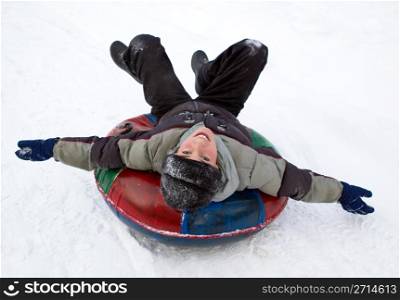 boy sledding down a snowy hill on a color inflatable sled